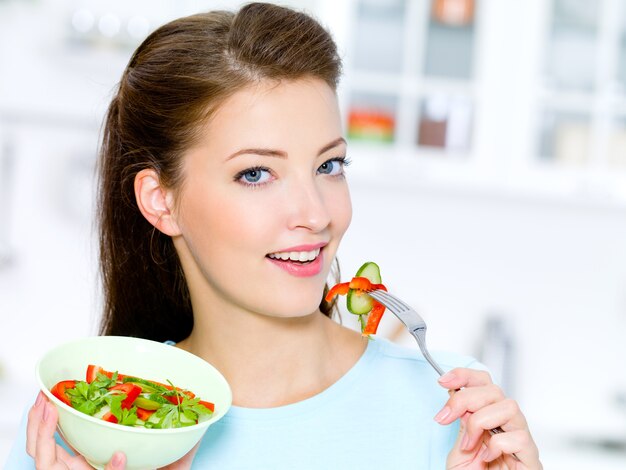 Gelukkige vrouw eet groentesalade in de keuken