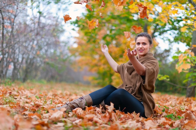 Gratis foto gelukkige vrouw gooit herfstbladeren