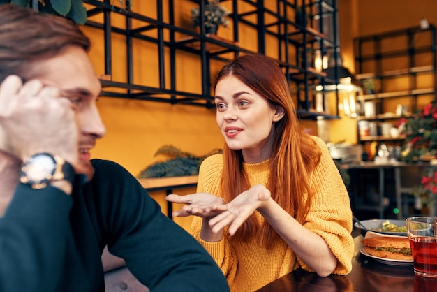 Gelukkige vrouw in een trui gebaren met haar handen leuke emoties en een man in een trui zit in een café