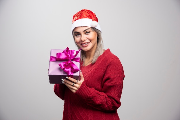 Gelukkige vrouw in kerstmuts die kerstcadeau aanbiedt.