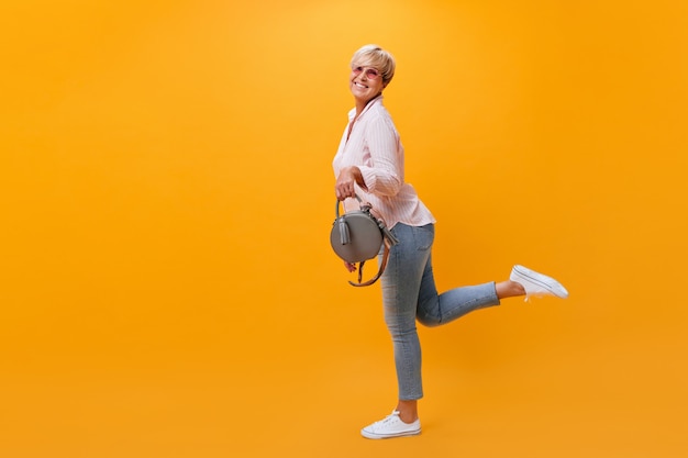 Gelukkige vrouw in spijkerbroek met plezier op een oranje achtergrond