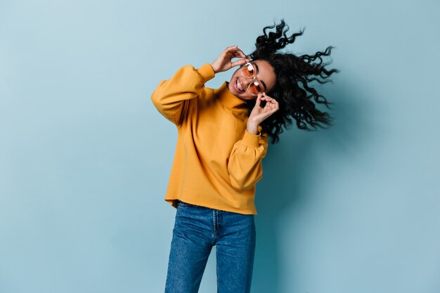 Gelukkige vrouw in vrijetijdskleding die op blauwe muur dansen