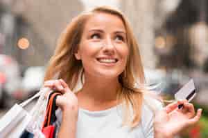 Gratis foto gelukkige vrouw met boodschappentassen in de ene hand en creditcard in de andere