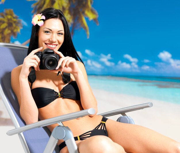 Gelukkige vrouw met een digitale camera die foto's op het strand neemt