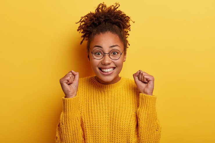 Gratis Foto gelukkige vrouw met knapperig haar, gebalde vuisten heft, voelt zich optimistisch als doel bereikt, breed lacht, heeft afro haar