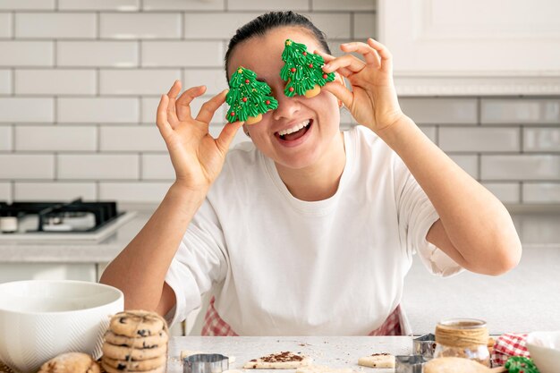 Gratis foto gelukkige vrouw met peperkoek in de vorm van kerstbomen in de keuken