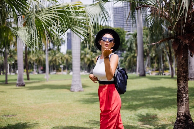 Gelukkige vrouw reizen rond Bangkok met rugzak, genieten van mooie zonnige dag in in tropisch park op groen grasveld