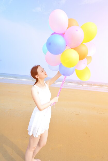 Gelukkige vrouw wandelen langs het strand met ballonnen