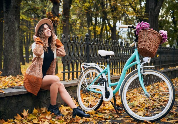 Gelukkige vrouw zitten in de buurt van fiets in stedelijk herfstpark