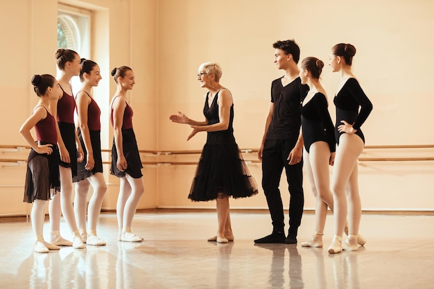Gratis foto gelukkige vrouwelijke balletinstructeur die met groep balletdanser communiceert vóór de repetitie bij dansstudio