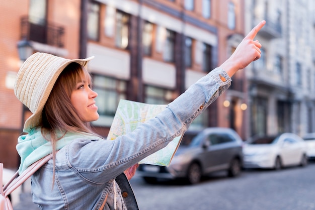 Gratis foto gelukkige vrouwelijke kaart van de reizigersholding het in hand richten op iets in de stad