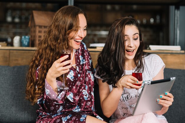 Gelukkige vrouwen met dranken die digitale tablet gebruiken