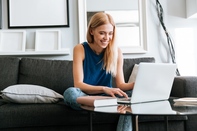 Gelukkige vrouwenzitting op bank en thuis het gebruiken van laptop