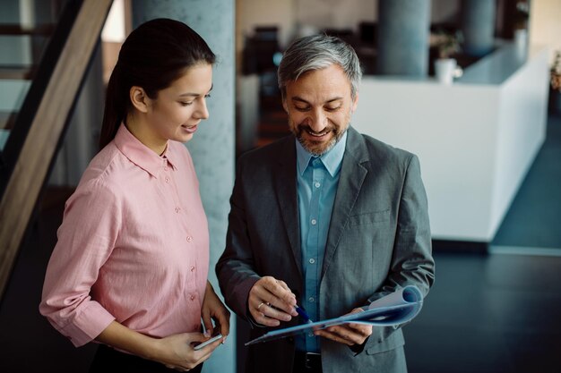 Gelukkige zakelijke collega's die samenwerken terwijl ze door het papierwerk in een gang gaan