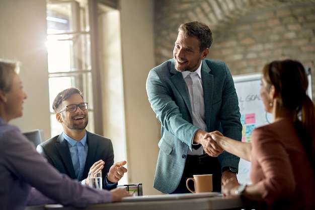 Gratis foto gelukkige zakenlieden die zijn collega's begroeten tijdens een vergadering en de hand schudden met een van hen op kantoor