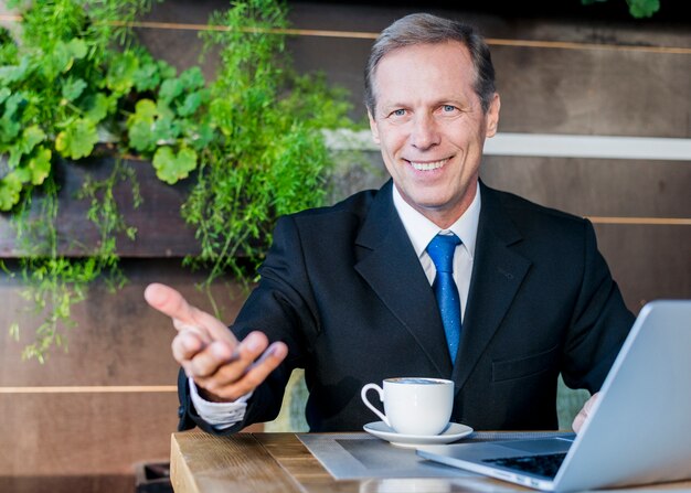 Gelukkige zakenman die handgebaar met kop van koffie en laptop op bureau maken