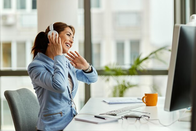 Gelukkige zakenvrouw die op een computer werkt en plezier heeft terwijl ze naar muziek luistert via een koptelefoon