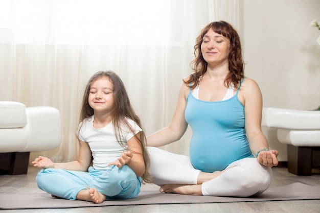 Gelukkige zwangere moeder en kind meisje mediteren samen thuis