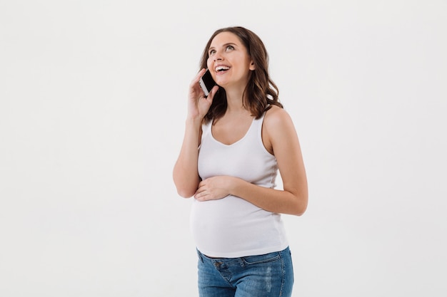 Gelukkige zwangere vrouw die door mobiele telefoon spreekt