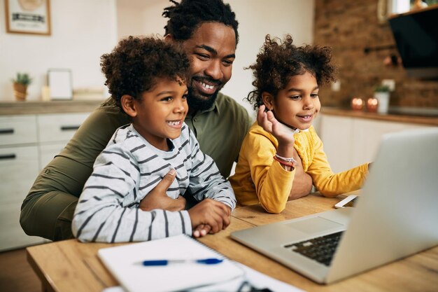 Gelukkige zwarte vader en kinderen die thuis videogesprek voeren via laptop