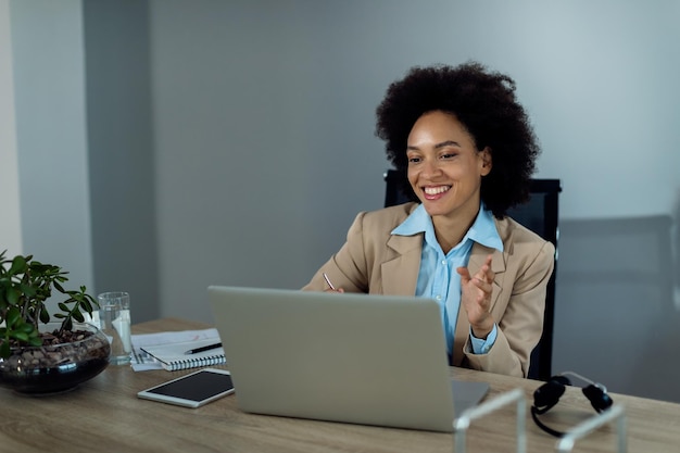 Gelukkige zwarte zakenvrouw die laptop gebruikt en videogesprek voert op kantoor