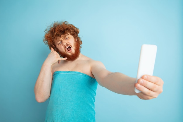 Gratis foto gelukkigste ochtend. portret van een jonge blanke man in zijn schoonheidsdag en huidverzorgingsroutine. mannelijk model met natuurlijk rood haar dat selfie in handdoek neemt. lichaams- en gezichtsverzorging, natuurlijk, mannelijk schoonheidsconcept.