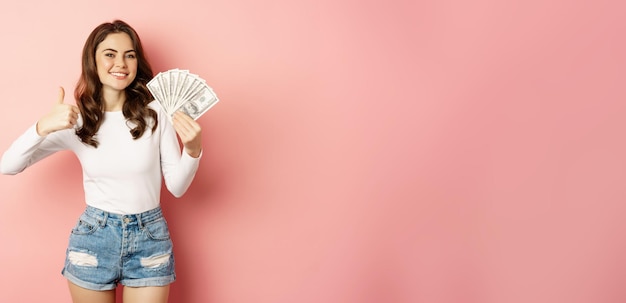 Gemakkelijk geld en leningsconcept glimlachende mooie vrouw die geld met tevreden gezicht toont dat duimen toont