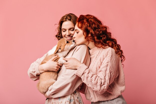 Gember vrouw kussende hond op roze achtergrond. Studio shot van prachtige meisjes poseren met puppy.