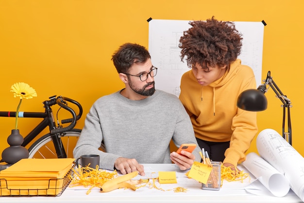 Gemengd ras vrouw en man collega's proberen een oplossing van werk te vinden controleer informatie op internet via mobiele telefoon studie papieren poseren in coworking space genieten van samenwerking