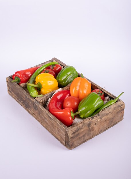 Gemengde chili pepers in een houten container op wit