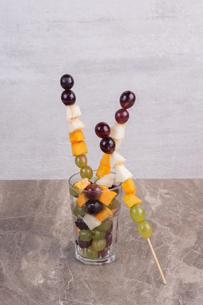 Gemengde fruitstokken in glas op marmeren tafel.