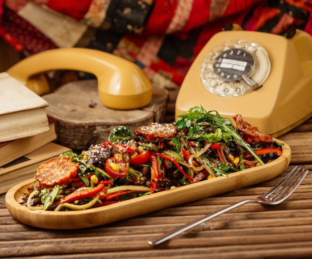 Gemengde gegrilde groentesalade met kruiden en olijfolie in houten plaat met een vintage rond telefoon.