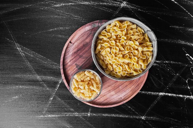 Gemengde pasta's in metalen kopjes op een houten schotel.