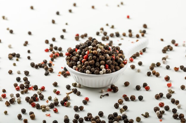 Gemengde peperbollen in een wit lepel zijaanzicht over kruidige en witte achtergrond