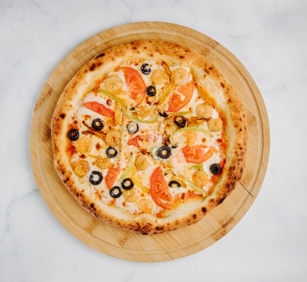 Gemengde voedselpizza met olijfbroodjes, groenten en gesmolten kaas op een rond houten bord.