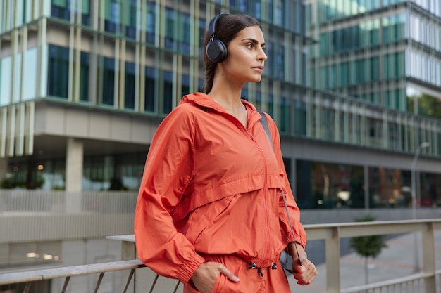 Gemotiveerde sportvrouw kijkt met vastberaden uitdrukking geniet van training buitenshuis heeft ochtendoefening routine gekleed in activewear luistert muziek poses in het centrum. Actief levensstijlconcept