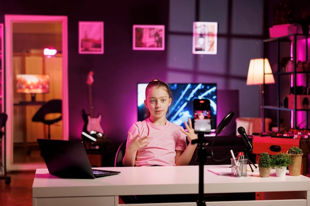 Gen Z entertainer gebruikt mobiele telefoon op driepoot stabilisator om inleidend segment te filmen voor vlog Jonge online ster in roze neon studio verwelkomt toegewijde fan community filmen met mobiele telefoon