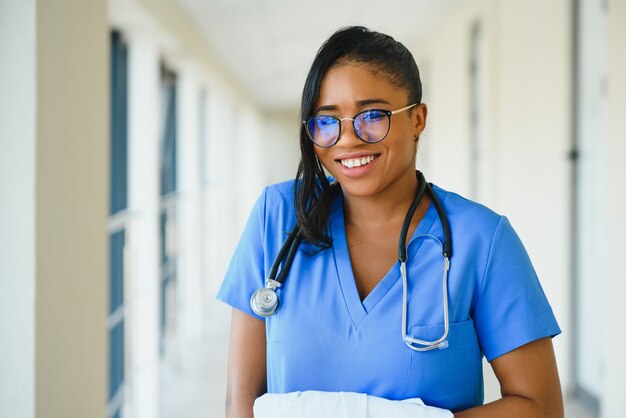 Geneeskunde, beroep en gezondheidszorg concept - gelukkig lachende afro-amerikaanse vrouwelijke arts met stethoscoop over ziekenhuis achtergrond