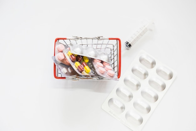 Geneeskundepillenpak in miniatuurboodschappenwagentje met spuit op witte achtergrond