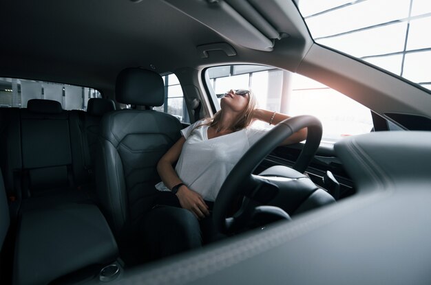 Genieten van comfortabel interieur. Meisje in moderne auto in de salon. Overdag binnenshuis. Een nieuw voertuig kopen