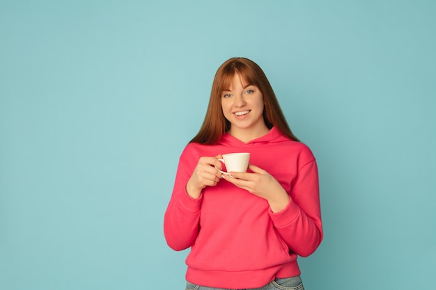 Genieten van koffie, thee. Portret van de blanke vrouw op blauwe studio oppervlak met copyspace.