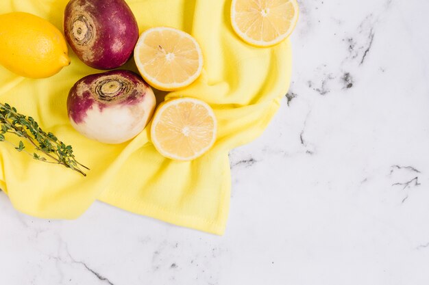 Geoogste rapen en gehalveerde citroenen op geel tafelkleed tegen witte marmeren achtergrond