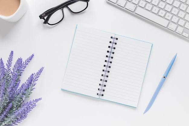 Gratis foto geopend notitieboekje dichtbij lavendel, toetsenbord en glazen op bureau