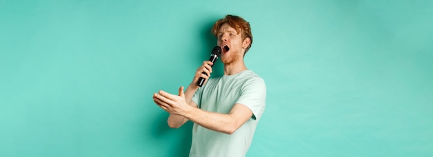 Gratis foto gepassioneerde roodharige man in t-shirt die serenade zingt met microfoon die opzij kijkt naar karaoke en gestu