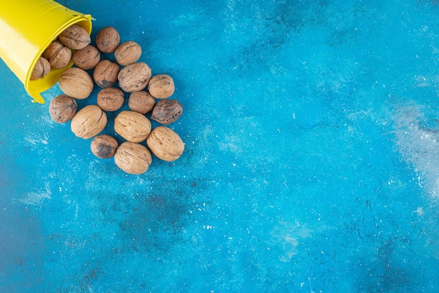Gepelde walnoten in een emmer, op de blauwe tafel.