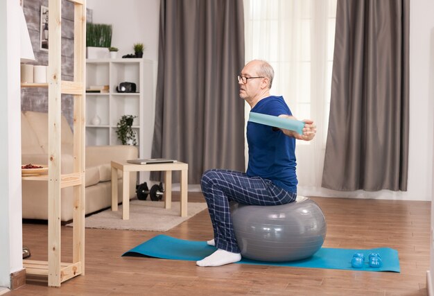 Gepensioneerde die sport met weerstandsband doet die op zwitserse bal zit