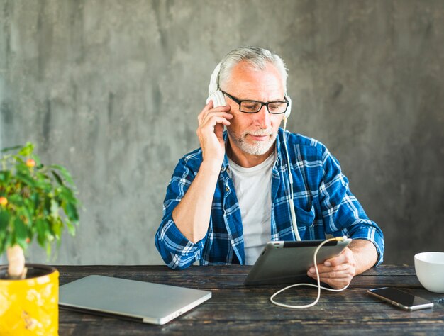 Gepensioneerde senior man luisteren muziek via hoofdtelefoon op tablet