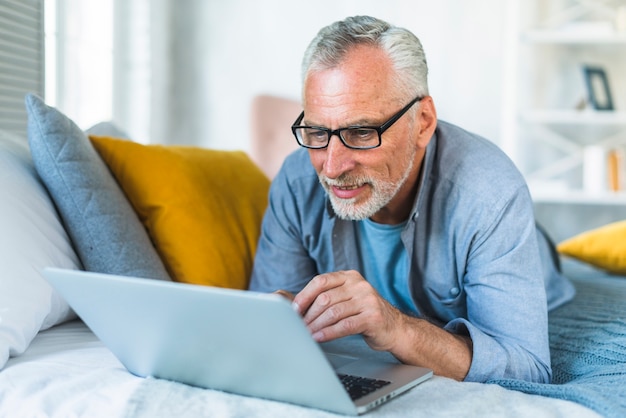 Gepensioneerde senior man ontspannen op bed te kijken naar laptop