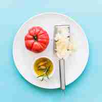 Gratis foto geraspte kaas met gehele rode tomaat en olie op witte plaat over de blauwe achtergrond