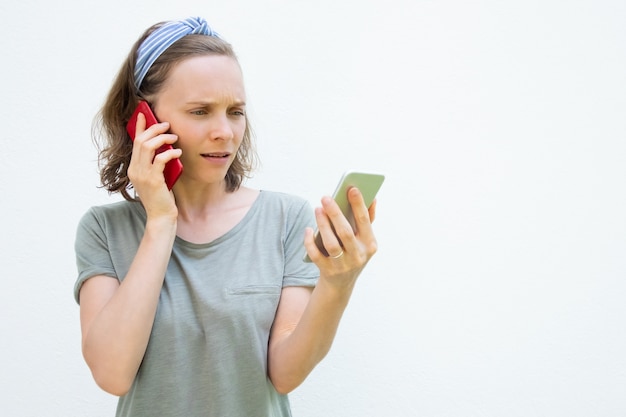 Gerichte drukke jonge vrouw met behulp van twee smartphones